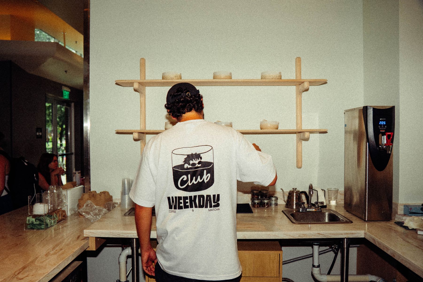 A Weekday barista in a Club Weekday shirt working at the back bar