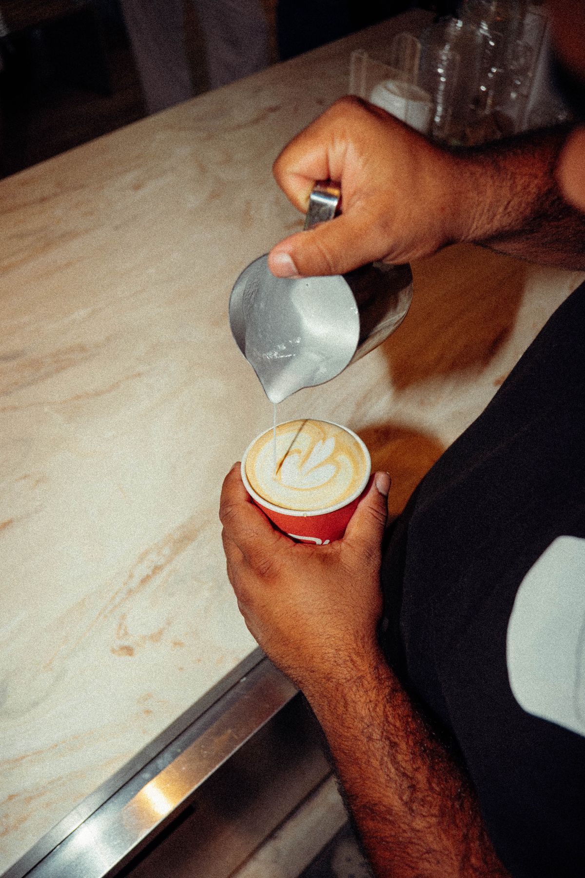 Barista pouring latte art into a red Weekday cup