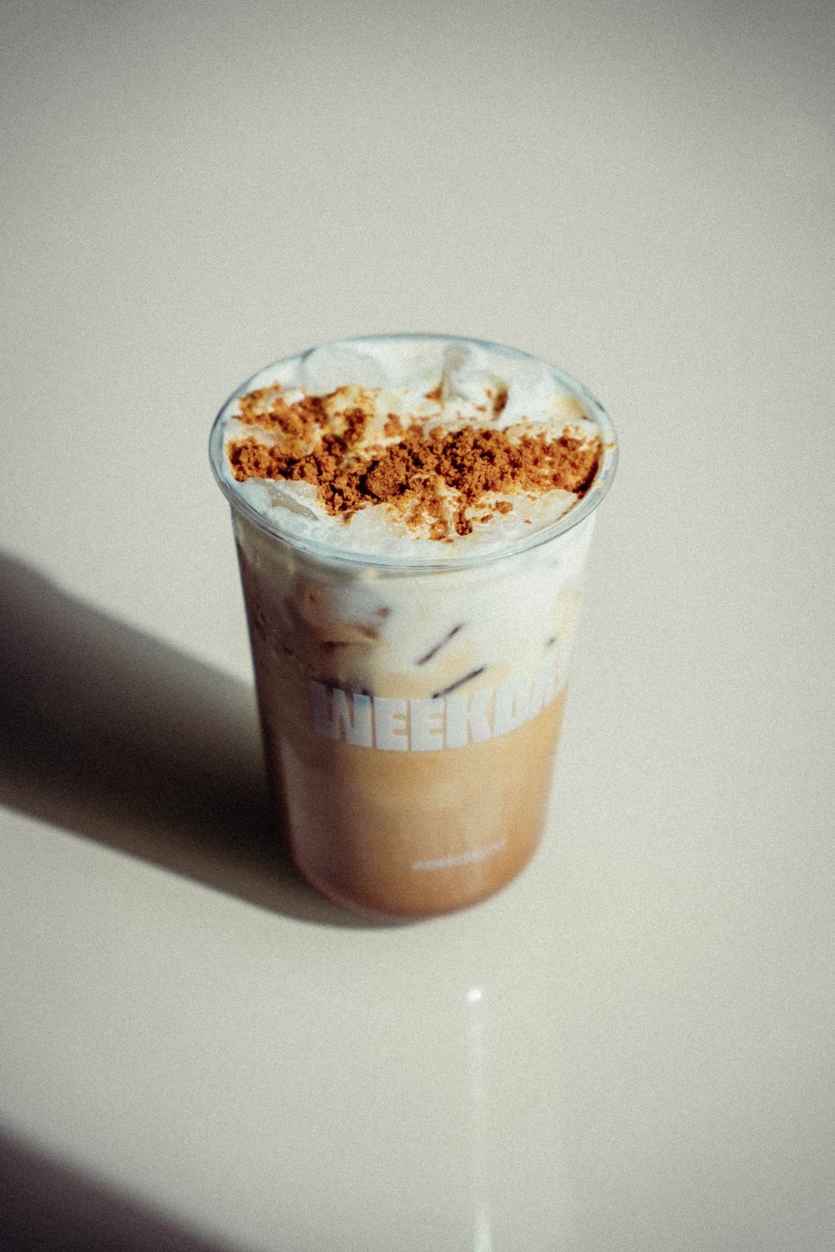 Iced Golden Shoyu latte in a Weekday cup topped with cookie crumble