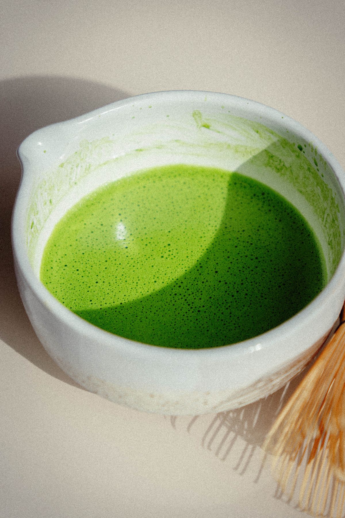 Freshly whisked matcha in a white bowl beside a bamboo whisk